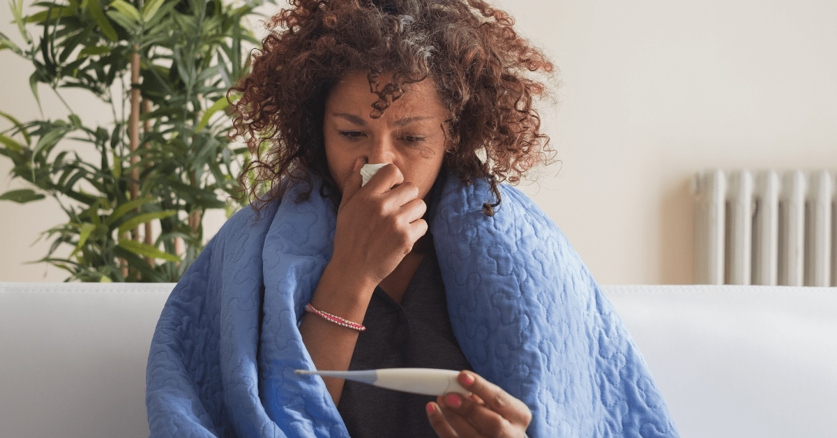 woman with flu blowing her nose and holding thermometer